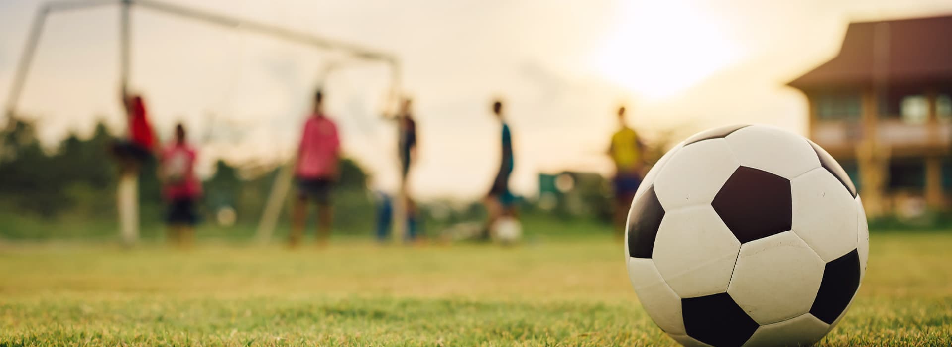 Fußball im Vordergrund auf Wiese, Tor und Mannschaft verschwommen im Hintergrund