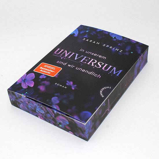 Das Buchcover zeigt … einen dunklen violett-schwarzen Hintergrund mit lila Blumen und dem großen Titel „UNIVERSUM“ in zartem Violett.