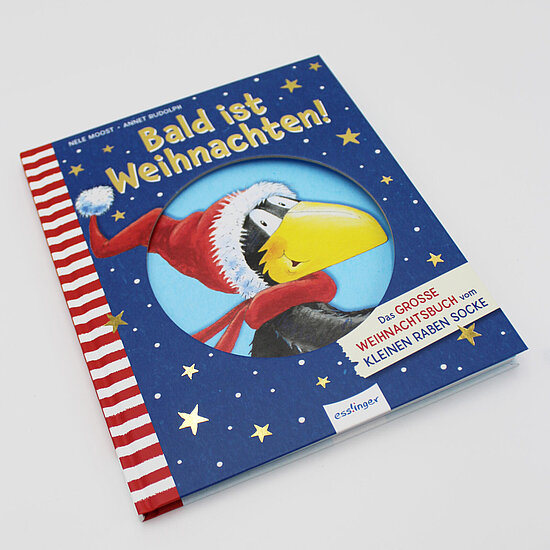 Das Buchcover zeigt einen schwarzen Raben mit roter Mütze und Schal und gelbem Schnabel vor blauem Sternenhimmel, rotweiß gestreiftem Rand.