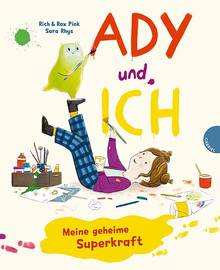 Das Buchcover zeigt ein Mädchen mit braunen, lockigen Haaren, das entspannt auf dem Boden liegt und malt. Neben ihr ist ein grünes, schelmisches Wesen, umgeben von Malutensilien und bunten Farben.