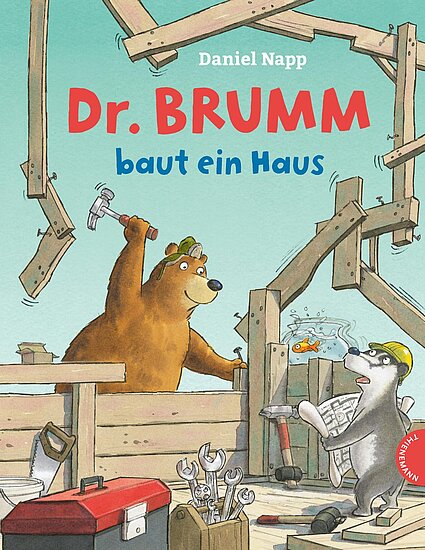 Das Buchcover zeigt einen braunen Bären mit einem Hammer in der Hand, der fröhlich in einem Baugerüst arbeitet, während ein grauer Dachs neugierig zuschaut. Der Hintergrund ist hellblau und zeigt einige Bauutensilien.