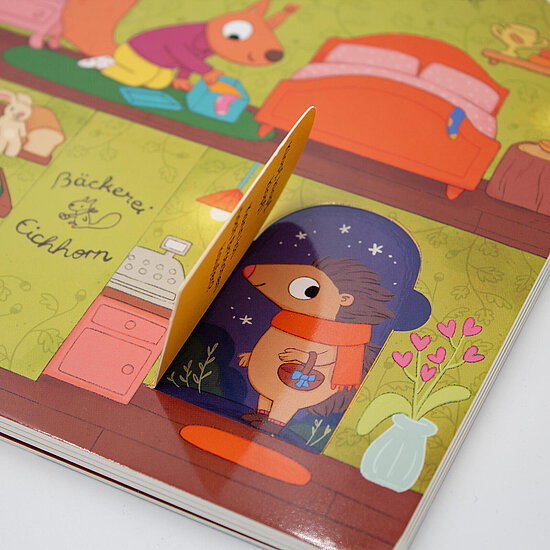 Das Buchcover zeigt einen Igel mit rotem Schal und Geschenk in einer blauen Tuer vor gruenem Wohnzimmer mit rosa Bett und Herzblumen.