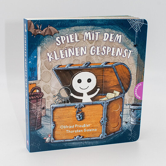 Das Buchcover zeigt ein weißes lächelndes Gespenst in einer offenen Holzkiste, vor blauviolettem Hintergrund mit Fledermaus und Spinnweben.
