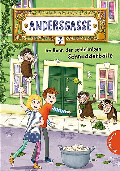 Das Buchcover zeigt einen bunten Straßenzug mit grünen Häusern. Zwei Kinder, ein Junge mit roten Haaren und ein Mädchen mit blonden Zöpfen, halten eine Schüssel mit runden, weißen Bällen, während fröhliche, kleine, affenähnliche Wesen um sie herumspielen.