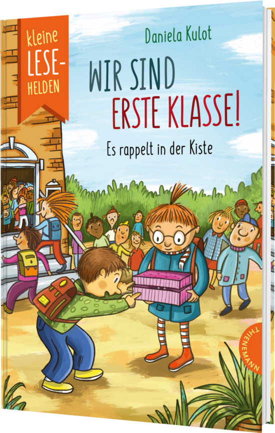 Das Buchcover zeigt fröhliche Kinder, die vor einer Schule stehen. Ein Junge mit Brille trägt eine Kiste, während andere Kinder neugierig zuschauen. Bunte Farben dominieren die Szene, die eine einladende Atmosphäre schafft.