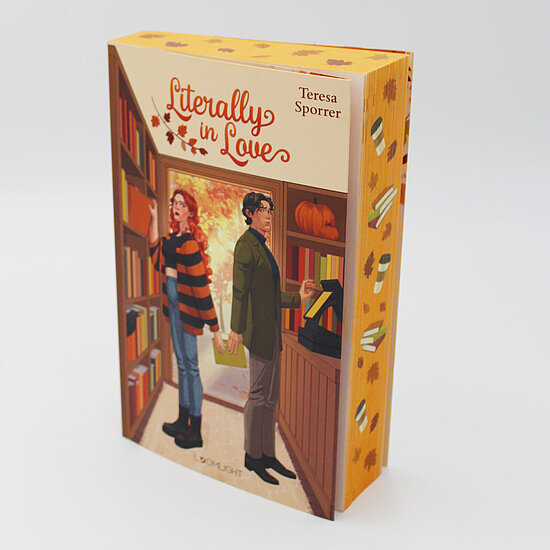 Das Buchcover zeigt … zwei Rücken an Rücken stehende Personen in einer warmen Herbstbuchhandlung mit Regalen, Büchern, einem Kürbis und orangen Blättern.