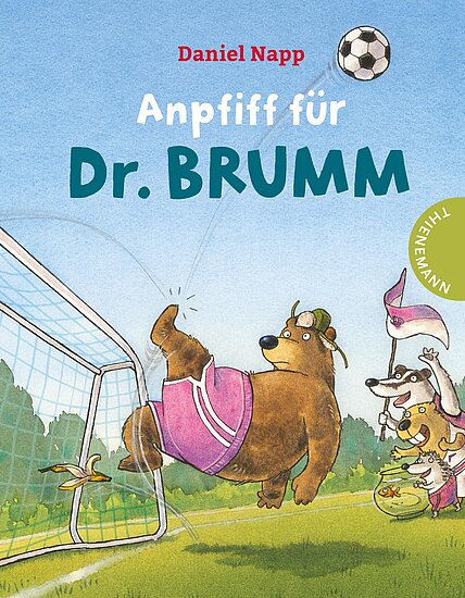 Das Buchcover zeigt einen spielenden Bären in pinken Shorts, der einen Fußball ins Tor schießt. Um ihn herum sind weitere Tiere, darunter ein Hund, auf einer grünen Wiese.