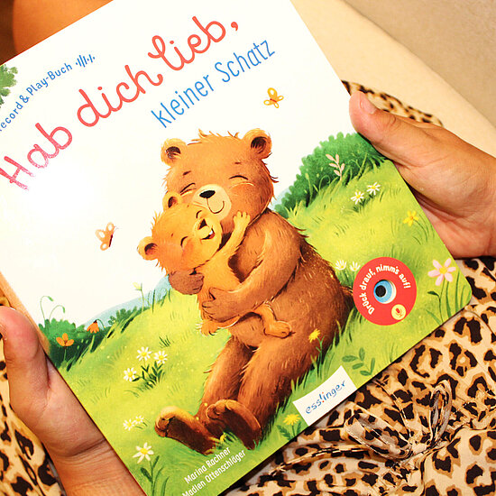 Das Buchcover zeigt ... zwei umarmende Baeren auf einer gruene Wiese mit weissen Blumen und zwei Schmetterlingen vor hellem Himmel.