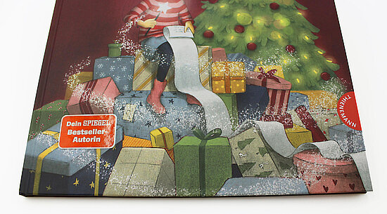 Das Buchcover zeigt ein Kind in gestreiftem Pullover über einem Sofa sitzend umgeben von bunten Geschenkpaketen und einem geschmückten Tannenbaum.