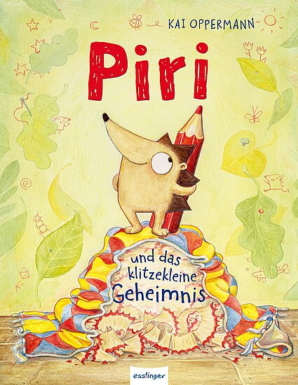 Das Buchcover zeigt das fröhliche Tier Piri, das als Bleistift verkleidet auf einem bunten Tuch steht. Im Hintergrund sind verspielte, stilisierte Pflanzen in sanften Farben zu sehen.