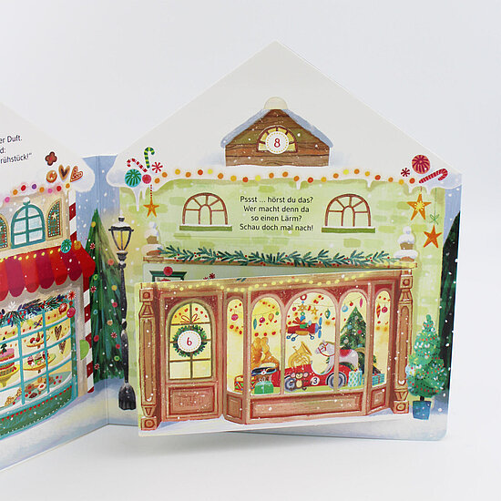 Das Buchcover zeigt ein festlich beleuchtetes Schaufenster eines Spielwarengeschäfts mit Spielzeugfiguren, Tannenbaum, Schnee und roten Akzenten.
