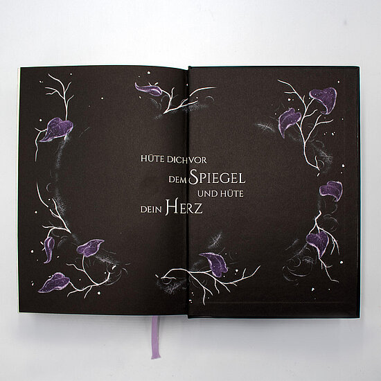 Das Buchcover zeigt ein schwarzes Layout mit ornamentalem Rahmen aus weissen Zweigen und violetten Blueten, zentrierter weisser Serifschrift.