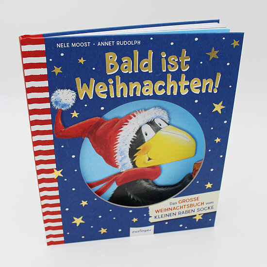 Das Buchcover zeigt einen fröhlichen schwarzen Raben mit großem gelbem Schnabel in roter Weihnachtsmütze und rotem Schal vor blauem Sternenhimmel.