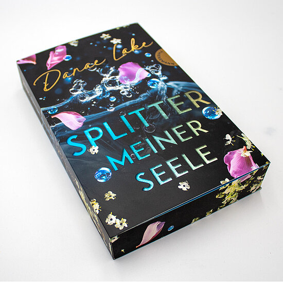 Das Buchcover zeigt auf schwarzem Grund eine Wasserfontaene mit blauen Tropfen, rosa Rosenblaettern, weissen Blueten und tuerkisfarbenem Titel.