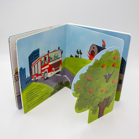 Das Buchcover zeigt ein aufgeschlagenes Pappbilderbuch mit rotem Feuerwehrauto vor blauen Häusern, brennender Scheune und grünem Apfelbaum.