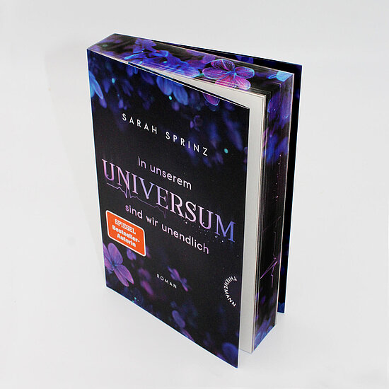 Das Buchcover zeigt den Titel in großen violetten Lettern und den Autorennamen vor einem dunkelblau violetten Hintergrund mit lila Blüten.